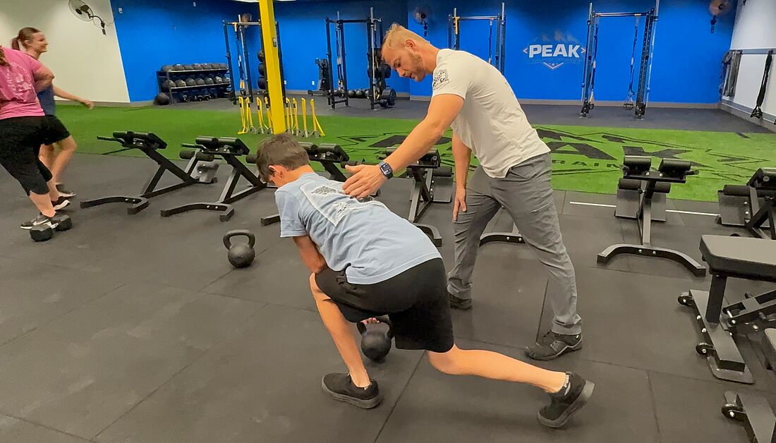 PEAK coach correcting an athlete’s kettlebell row form